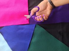 a person holding a pair of scissors in front of several colored pieces of fabric that have been folded together