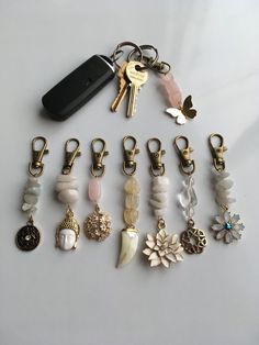 a collection of key chains and charms on a white surface with a cell phone in the background