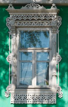 an old window on the side of a green building with a tree reflected in it