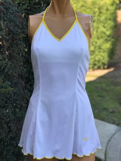 a female mannequin wearing a white tennis dress with yellow piping on the sides