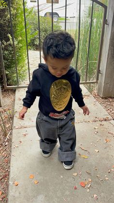 a little boy standing on top of a sidewalk next to a metal fence and holding onto a gold plate