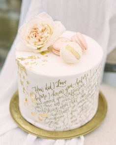 a white cake with gold lettering and flowers on top is sitting on a table in front of a person