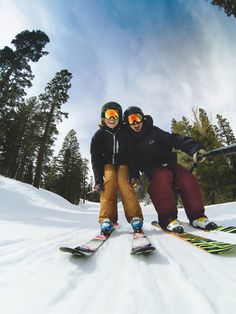 two people on skis posing for a photo in the snow with trees behind them