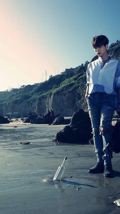 a man standing on top of a sandy beach next to the ocean holding a bag