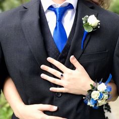 a man wearing a blue tie and matching boutonniere with his hands on his chest