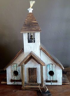 a small white church with bells on it's roof and bell tower, sitting on a wooden table