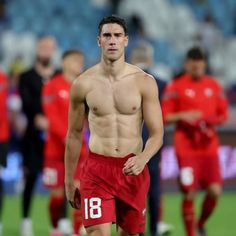 a shirtless male soccer player walking on the field with his team mates in the background