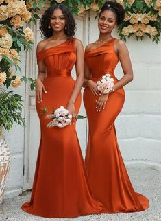 two women in orange dresses standing next to each other with flowers on the wall behind them