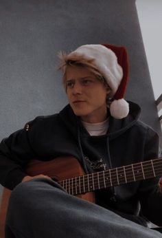 a young man wearing a santa hat while playing an acoustic guitar