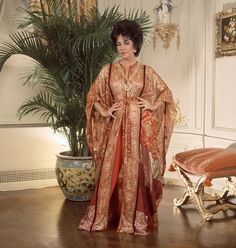 a woman in an orange and gold dress standing next to a potted plant