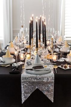 the table is set with black and white dishes, silver napkins, candles, and plates