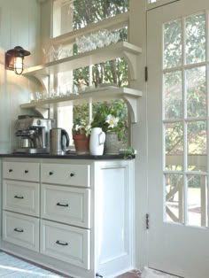 a kitchen with white cupboards and glassware on the top shelf next to an open door