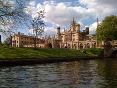 a large building sitting on top of a lush green hillside next to a river under a blue cloudy sky