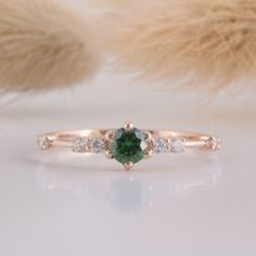 a ring with a green stone surrounded by three diamonds on top of a white surface