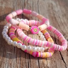 three bracelets with pink, yellow and white beads on top of a wooden table