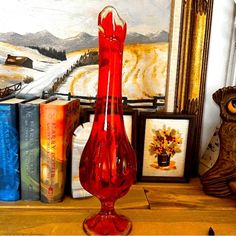 a red vase sitting on top of a wooden table next to books and an owl