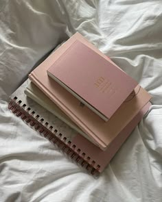 two notebooks sitting on top of each other on a white sheet covered bed with sheets