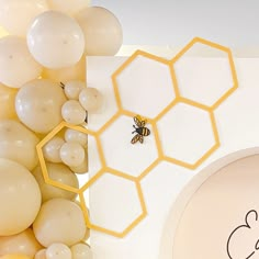 a bee sitting on top of a table surrounded by balloons and honeycombs in the background