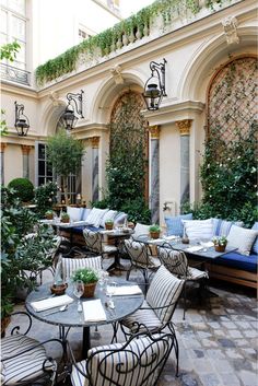 an outdoor seating area with potted plants on the tables and chairs in front of it