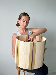 a woman sitting on a stool holding a lamp shade