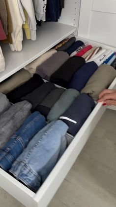 a person standing in front of a white closet filled with pants and sweaters on hangers