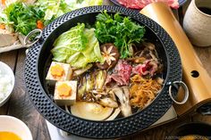 a bowl filled with lots of food on top of a wooden table next to bowls and utensils