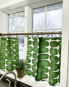 a kitchen sink under a window next to a green curtain with leaves on it and a potted plant