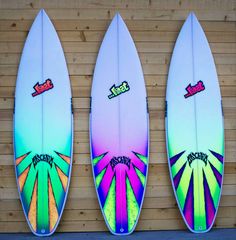 three surfboards are lined up against a wooden wall