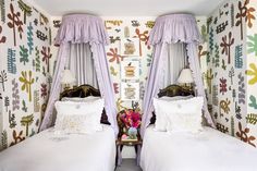 two beds with white covers and purple drapes in a room decorated with wallpaper