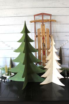 three wooden christmas trees in front of a sled and rocking chair on a table