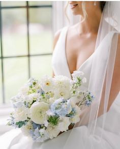 a bride holding a bouquet of white and blue flowers on her wedding day in front of a window