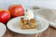 a piece of cake sitting on top of a white plate next to two red apples