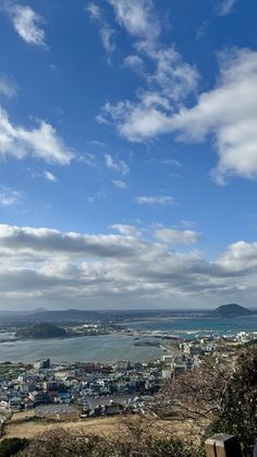 a view of the ocean from atop a hill with clouds in the sky above it