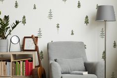 a living room with a chair, bookshelf and wallpaper that has trees on it