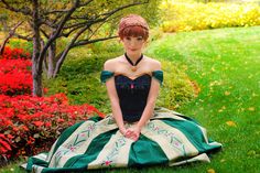 a woman in a green and white dress sitting on the ground next to some flowers