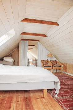 an attic bedroom with wood floors and white bedding, along with a rug on the floor