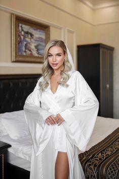 a woman standing in front of a bed wearing a white robe