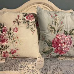 two pillows with pink flowers on them sitting next to each other in front of a blue wall