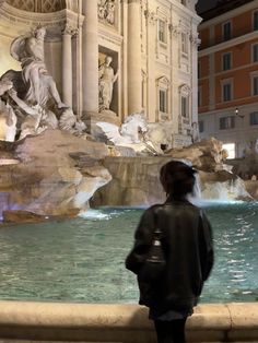 a person standing in front of a fountain with statues on the sides and water flowing from it