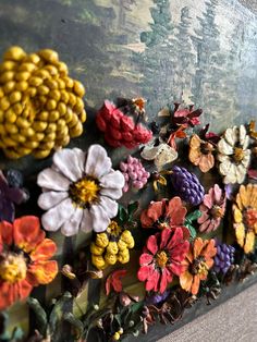 an assortment of colorful flowers on display in front of a large piece of art work