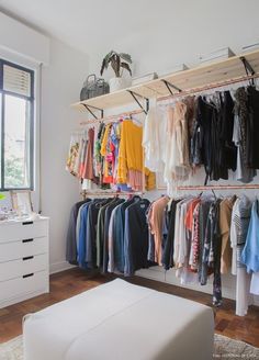 an organized closet with clothes hanging on the wall, and a white ottoman in front of it