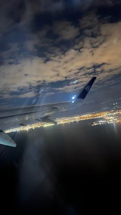 the wing of an airplane as it flies over a city at night with lights in the distance