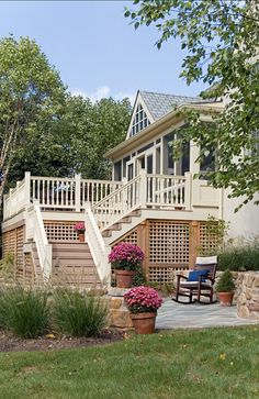 a house with stairs leading up to the front door and deck area, surrounded by flowers