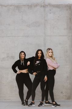 three women standing next to each other in front of a cement wall with their hands on their hips