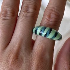 a woman's hand with a green and black striped ring on her left finger