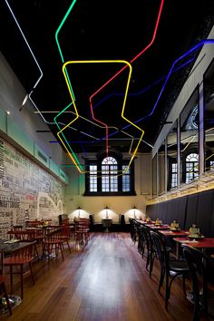 an empty restaurant with tables and chairs lit up by neon colored lights hanging from the ceiling