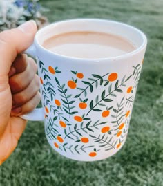 a hand holding a coffee cup with oranges painted on the outside and green leaves