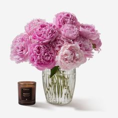 a glass vase filled with pink flowers next to a jar of wax and a candle