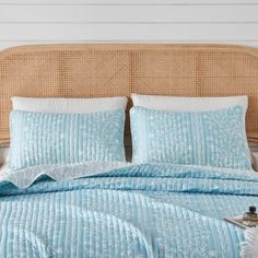 a bed with blue comforter and pillows on it in a bedroom next to a wicker headboard