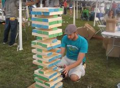 a man kneeling down next to a tall tower made out of wooden blocks on top of grass